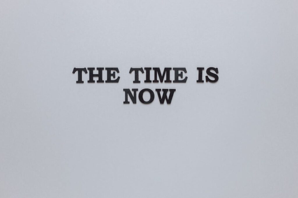 Minimalist poster with the motivational quote 'The Time is Now' on a gray background.