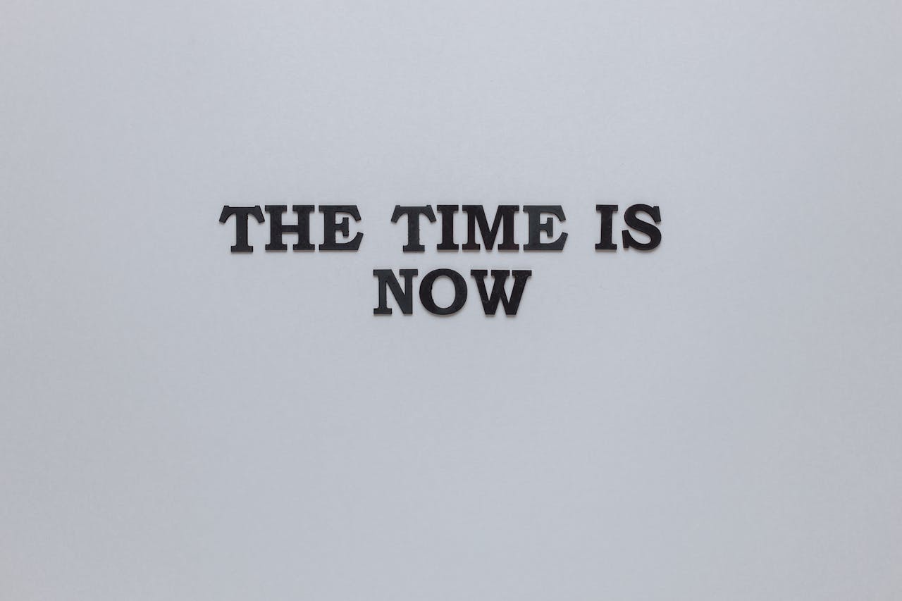 Minimalist poster with the motivational quote 'The Time is Now' on a gray background.